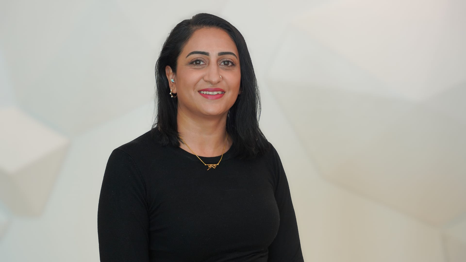 Lady smiling in black shirt in front of while wall