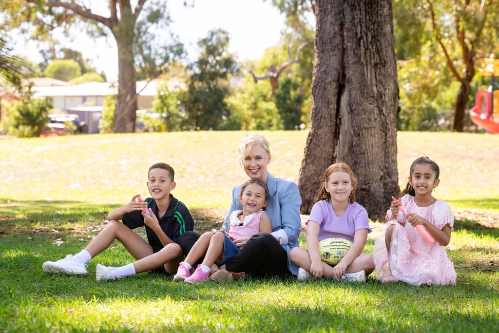 Jackie Davis sitting down in grass with a little girl in her lap and kids sitting next to her smiling.